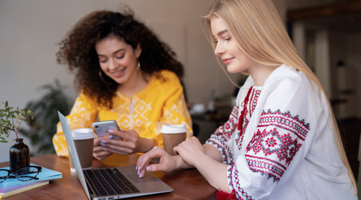 Duas profissionais interagindo com notebook e celular em um trabalhando em um café, representando o conceito de social selling e construção de conexões no ambiente digital.