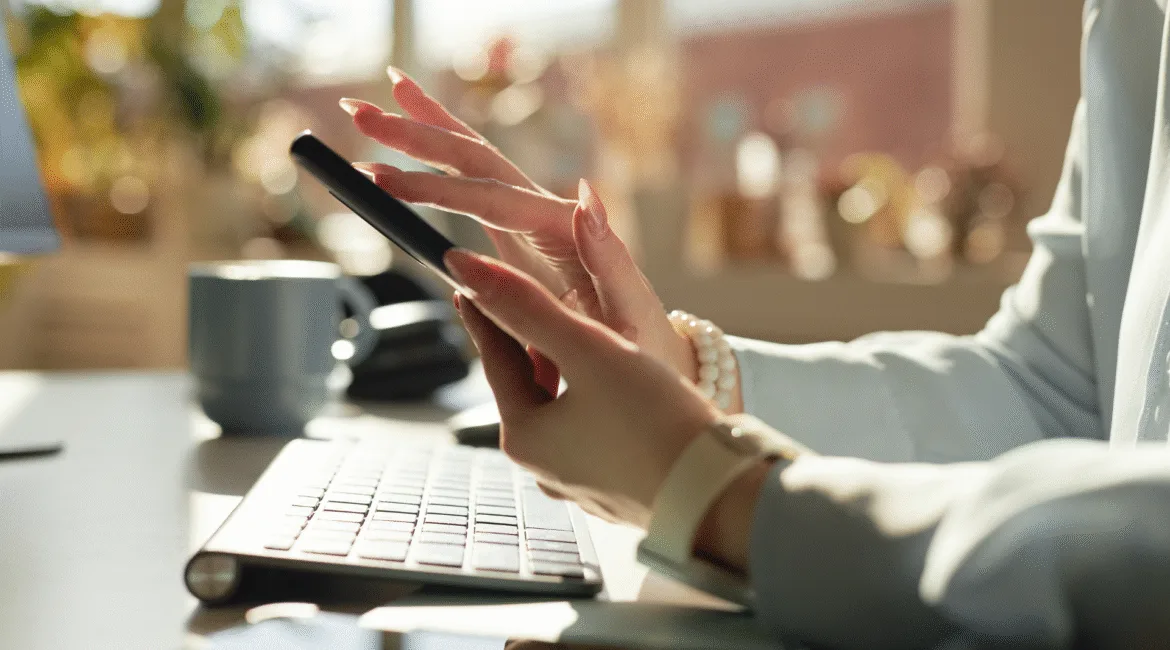 Mulher usando o celular para atualizar as redes sociais em um ambiente de trabalho corporativo.