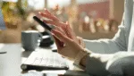 Mulher usando o celular para atualizar as redes sociais em um ambiente de trabalho corporativo.