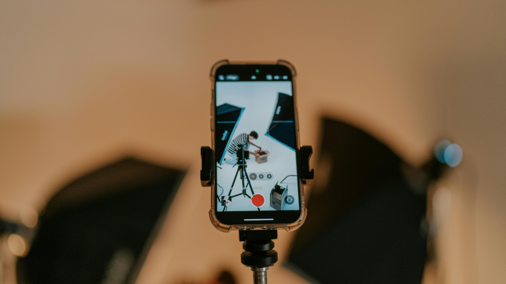 Smartphone preso a um tripé gravando a criação de conteúdo em estúdio, com câmera apontada para um setup de filmagem, representando o trabalho de marcas e criadores digitais.