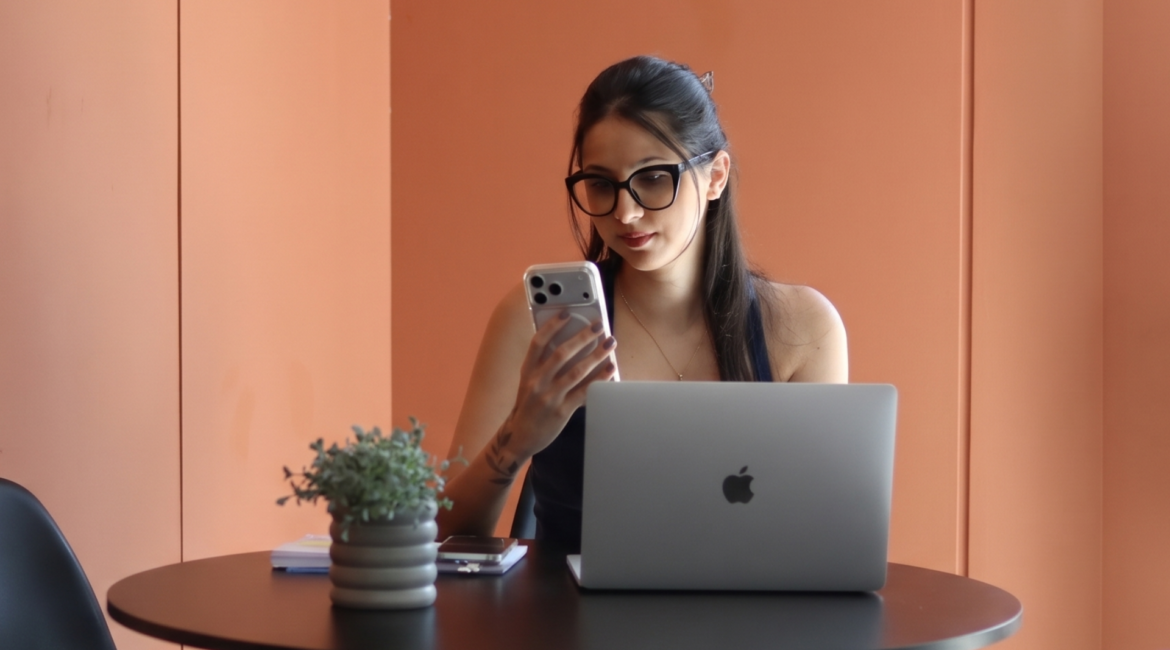 Mulher utilizando celular e notebook em ambiente de trabalho, representando estratégia de conteúdo que vende e presença digital para negócios.
