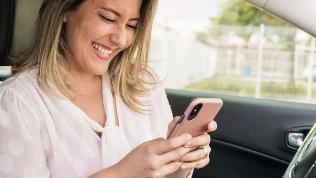 Lady Drive representada por mulher sorrindo enquanto usa o celular dentro do carro.